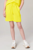 Girl wearing bright yellow drawstring shorts and sneakers, athleisure summer outfit