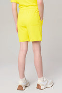 Girl wearing bright yellow athletic shorts and sneakers, standing with hands in pockets