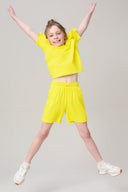 Girl jumping in bright yellow athletic summer shorts and tee, white sneakers, studio background