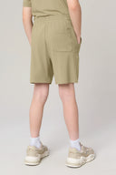 Boy wearing light olive athleisure shorts with pocket, white socks, and beige sneakers