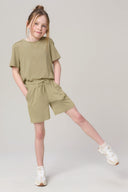 Girl wearing light olive green athletic T-shirt and drawstring shorts with white sneakers