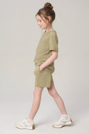 Girl wearing matching willow green athleisure shorts and t-shirt set, white sneakers