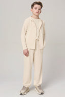 Boy wearing sand beige kids UV hoodie and matching pants, standing in studio