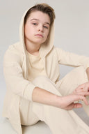 Boy wearing sand-colored kids UV hoodie and pants, seated on light background
