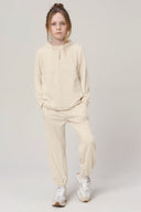 Girl wearing sand-colored kids UV hoodie and joggers, standing in a studio