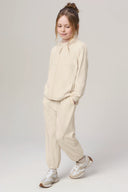 Girl wearing a light sand kids UV hoodie and matching joggers, standing in a studio.