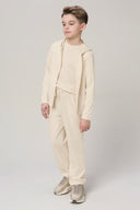 Boy in sand-colored kids jogger set with hoodie and sneakers, standing indoors