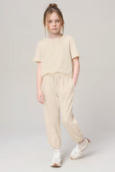 Girl wearing sand-colored jogger pants and matching t-shirt, hands in pockets, white sneakers