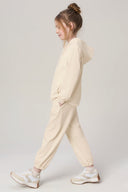 Girl in sand beige kids jogger set with hooded sweatshirt and white sneakers walking sideways