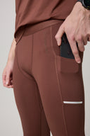 Brown athletic tights with side pocket holding a phone, close-up of fit and stitching detail
