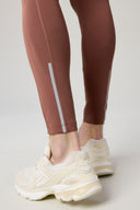 Close-up of brown athletic tights with reflective stripe detail and cream running shoes