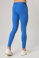 Man wearing cobalt blue athletic tights with pockets and white sneakers, rear view