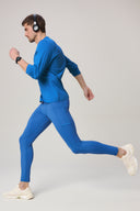 Man running in cobalt blue athletic tights, blue top, and sneakers against neutral background