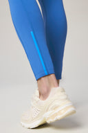 Close-up of cobalt blue athletic tights with light blue stripe and cream sneakers