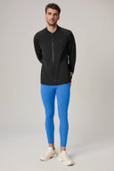 Man in charcoal fitted athletic jacket and bright blue leggings, studio background
