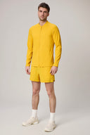 Man wearing a bright yellow fitted athletic jacket and shorts set, standing indoors.