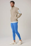 Man wearing beige zip-up jacket with white arm pocket and bright blue athletic leggings