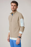 Man wearing a beige zip-up athletic jacket with arm pocket and blue leggings