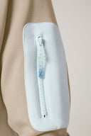 Close-up of light beige athleisure jacket sleeve with white zippered pocket detail.
