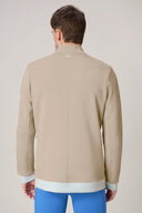 Back view of a man in a beige athletic jacket with white cuffs, blue leggings