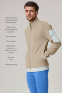 Man wearing beige athleisure jacket with zip pocket and blue leggings, studio background.