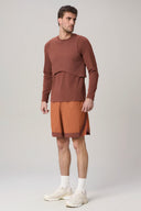 Man wearing brown long-sleeve top and rust athletic shorts with white sneakers.