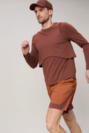 Man in brown athletic wear and orange running shorts, mid-stride, neutral background