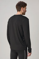Man wearing charcoal long sleeve active tee, back view, in minimalist setting