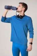 Man wearing cobalt blue long sleeve active tee and leggings, drinking from water bottle