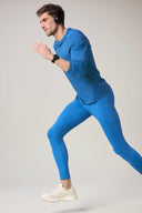 Man running in cobalt blue athletic top and leggings, wearing headphones, fitness apparel