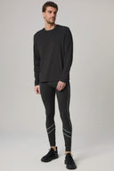 Man modeling charcoal reflective leggings with side stripes and black long sleeve shirt