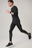 Man running in charcoal zebra reflective leggings with black athletic shoes against a neutral background