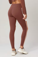 Back view of sepia brown leggings with white side stripes, worn by a model standing indoors