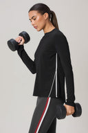 Woman in black long sleeve athletic shirt and striped leggings lifting dumbbells