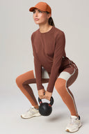 Woman in brown long sleeve activewear squatting with a kettlebell in studio
