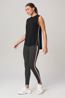 Woman wearing sleeveless charcoal active top and striped black leggings, white sneakers