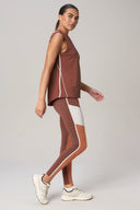 Woman in sepia sleeveless active top and colorblock leggings, side view, neutral background