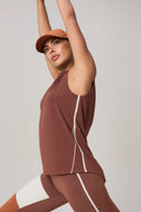 Woman stretching in sleeveless sepia activewear top, matching leggings, and orange cap