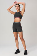 Woman modeling charcoal bike shorts and matching crop top with striped trim, activewear set