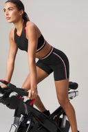 Woman in charcoal bike shorts and crop top riding stationary bike, activewear studio shot