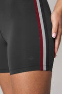 Charcoal bike shorts with side red and gray stripes, close-up on leg and hand