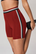 Woman wearing merlot red bike shorts with black and grey side stripe, stretching leg