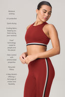 Woman wearing a merlot red sports bra and leggings with black and white stripes, featuring moisture wicking, UV protection, odor control, and 4-way stretch properties.
