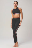 Woman wearing charcoal mid impact sports bra and matching high-waisted leggings with red and white stripes.