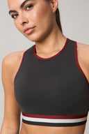 Woman wearing charcoal high-neck sports bra with burgundy trim and striped band