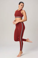 Woman in merlot athletic bra and matching leggings with stripe, standing on one foot