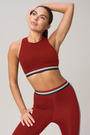 Woman wearing red mid-impact sports bra and leggings with black and white striped band
