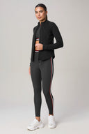 Woman wearing charcoal athletic jacket, matching leggings with side stripes, and white sneakers