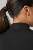 Close-up of woman wearing charcoal athletic jacket with ponytail and minimal logo on collar