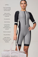Woman wearing short-sleeve zip-up rash guard, color-blocked black and gray, holding gym bag